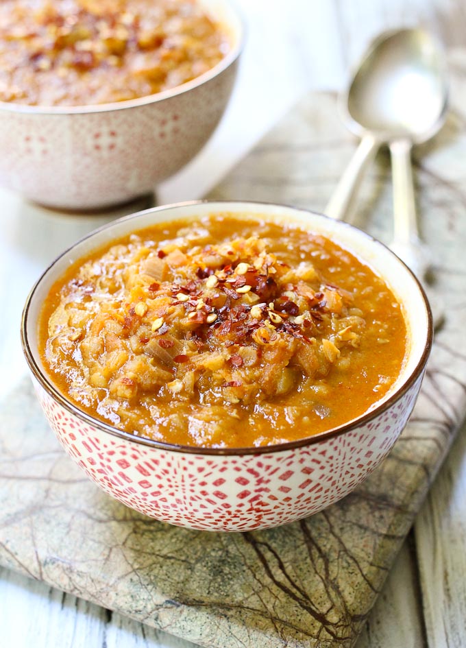 Spicy red lentil soup in a bowl. Two spoons and another bowl in the background.