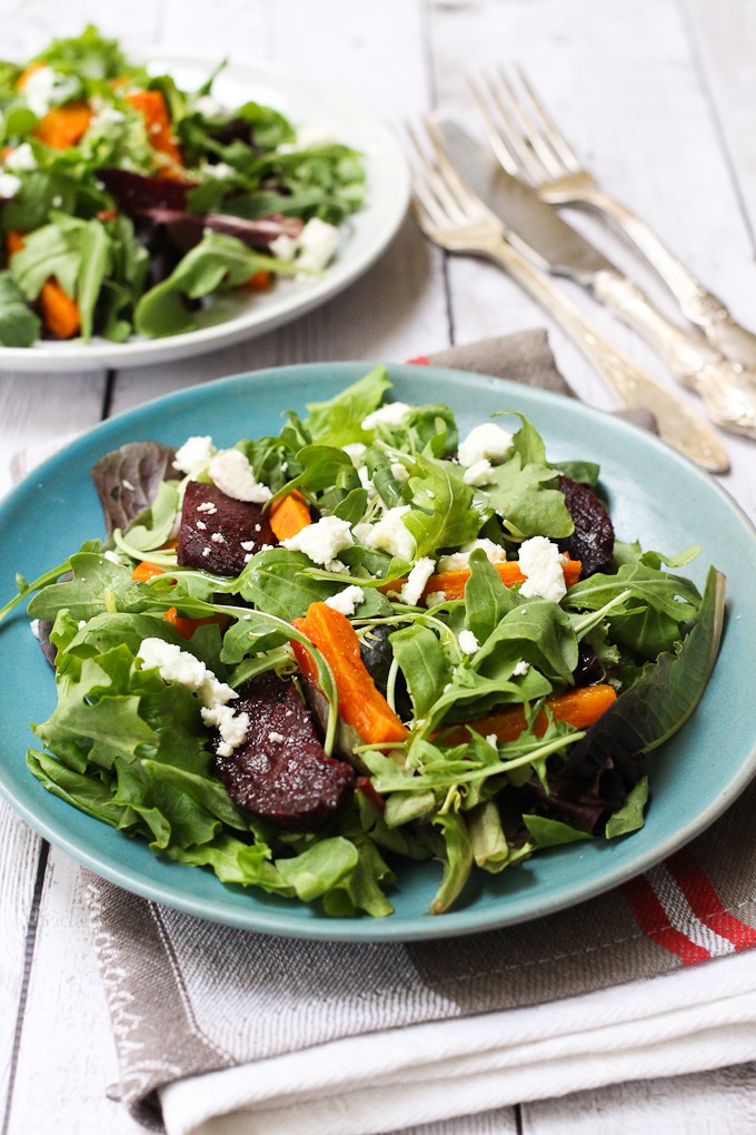 Mixed Greens Salad topped with roasted veggies and goat cheese, served on a blue plate.