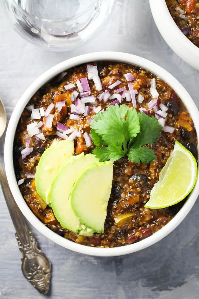 Quinoa chili in a bowl garnished with red onion, avocado, cilantro, and lime.