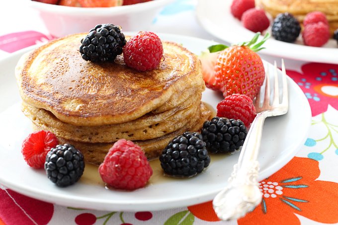 Buttermilk pancakes made with spelt flour on a white plate, garnished with berries and maple syrup.