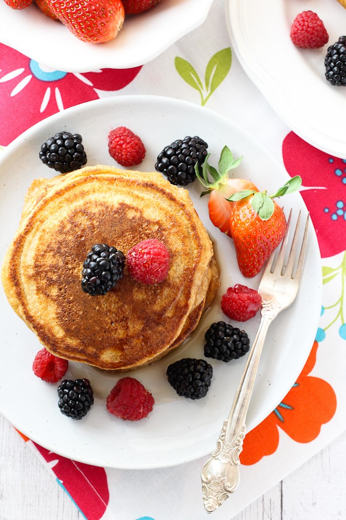 Overhead shot of spelt pancakes on a white plate, garnished with berries. Silver fork to the right. 