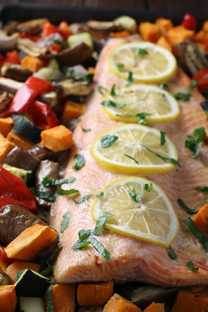 Baked rainbow trout with chopped vegetables, garnished with lemon slices.