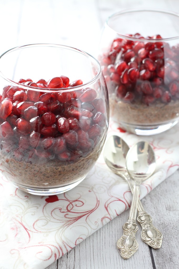 Chocolate chia pudding in glasses garnished with pomegranate. Two silver spoons to the right.
