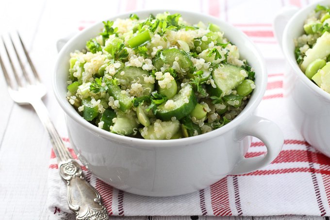 Green quinoa salad in a white bowl with a silver fork on the left.