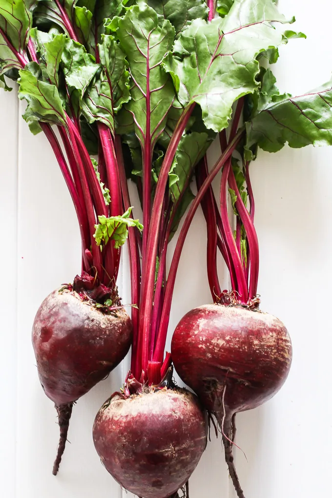 Three red beets with green tops laying on a white back ground.