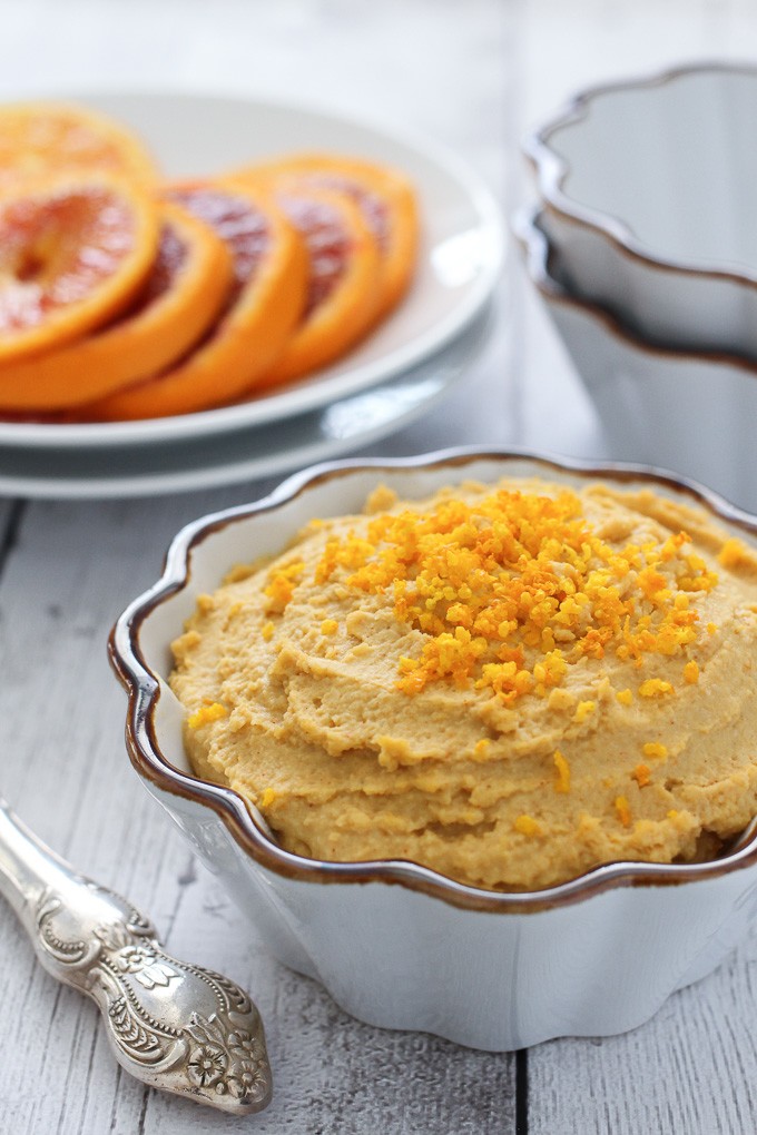 Orange hummus in a bowl garnished with grated orange rind.