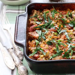 Chicken and lentils in a baking dish. Garnished with chopped parsley. Silver cutlery to the left.