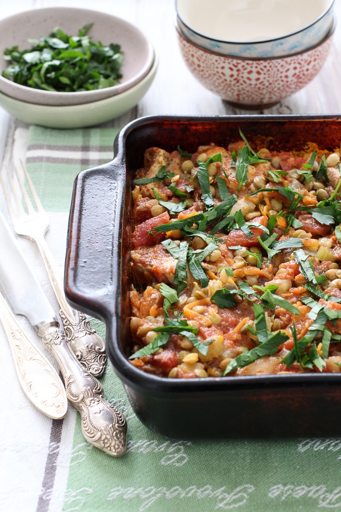 Chicken and lentils in a baking dish. Garnished with chopped parsley. Silver cutlery to the left.