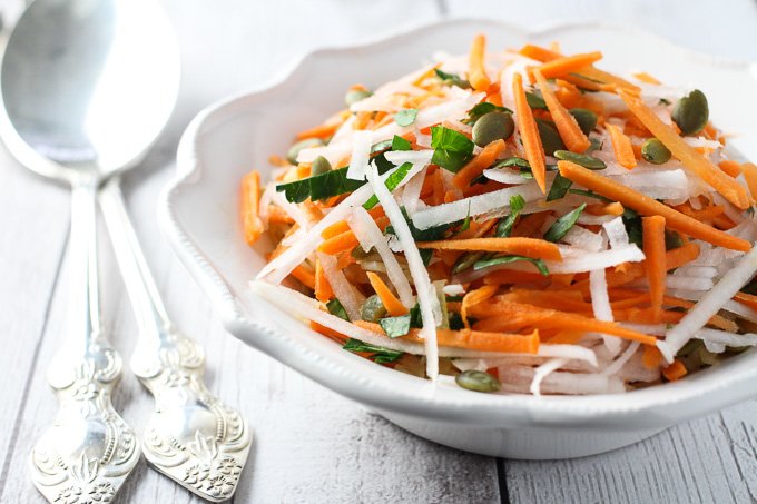 Raw turnip salad on a white plate with silver spoons to the left.