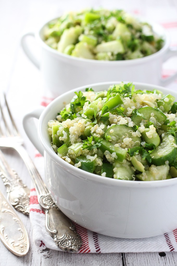 Green quinoa salad in white bowls. Silver forks on the left side.