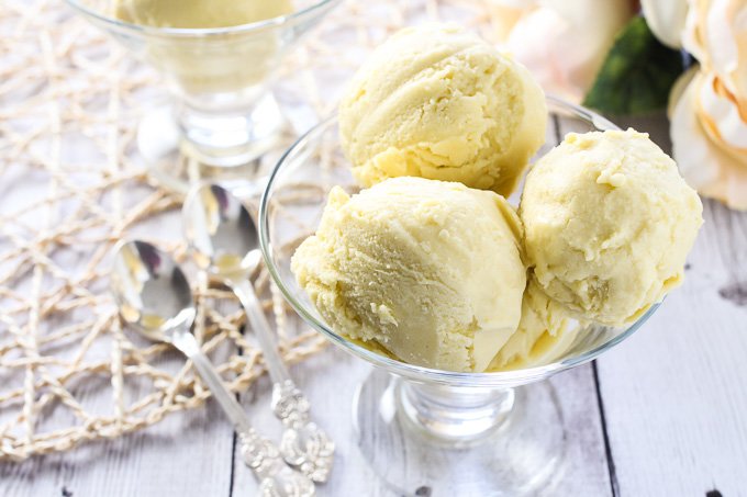 Vegan mango ice cream in a glass bowl with 2 silver spoons to the left.