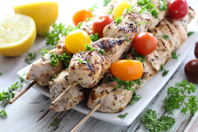 Chicken kebabs on a plate garnished with chopped parsley and cherry tomatoes.