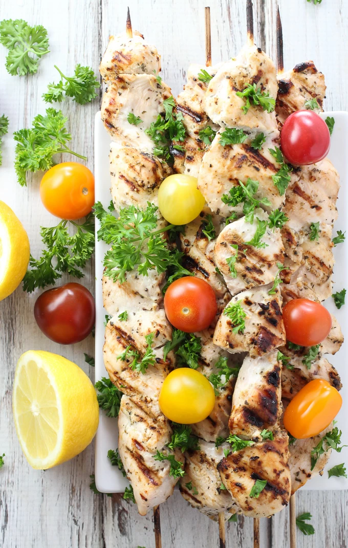Grilled yogurt marinated chicken kebabs on skewers, garnished with cherry tomatoes and parsley. Top view.