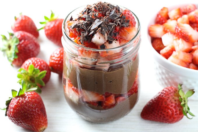 Chocolate mousse without eggs in a jar with whole strawberries around it. Side view.