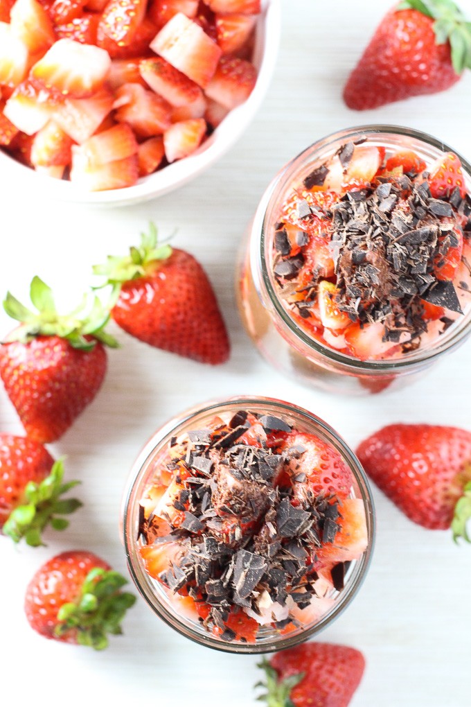 Coconut milk chocolate pudding in jars with strawberries laying around them. Top view.