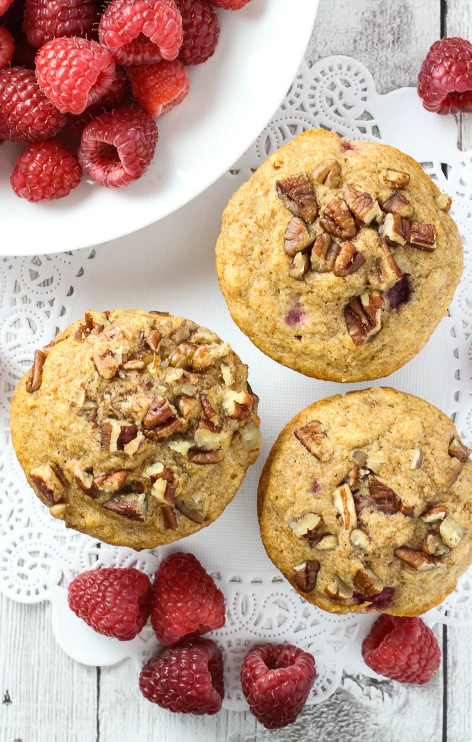 Top view of the spelt muffins and fresh raspberries which are arranged around them.