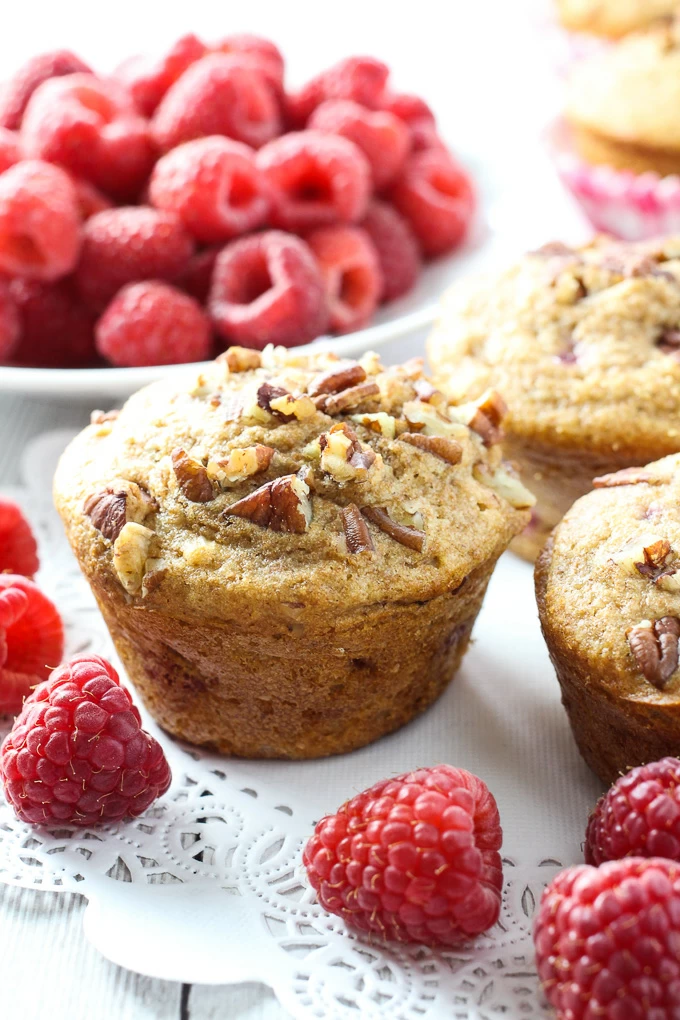 Spelt raspberry muffins on white background with whole raspberries around them.