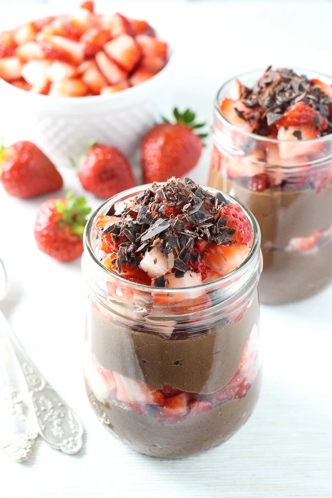 Two glass jars with the chocolate mousse. Strawberries in the background.