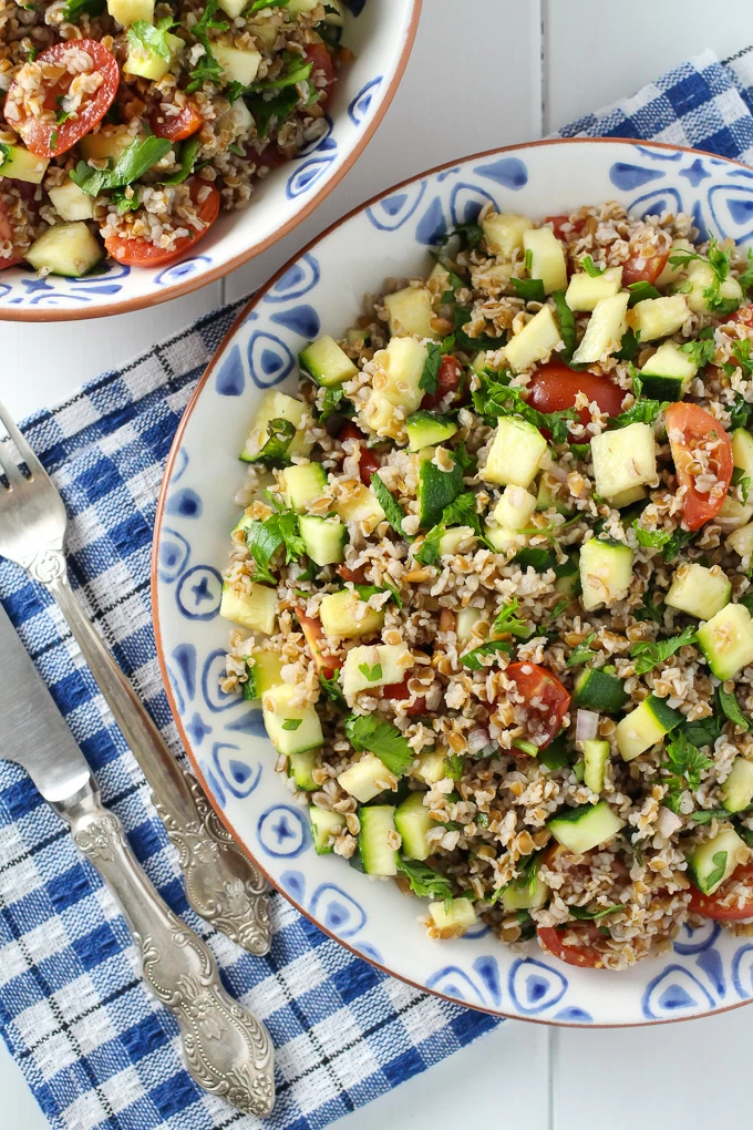 Zucchini tabbouleh salad on a plate with a fork and knife to the left. Top view.