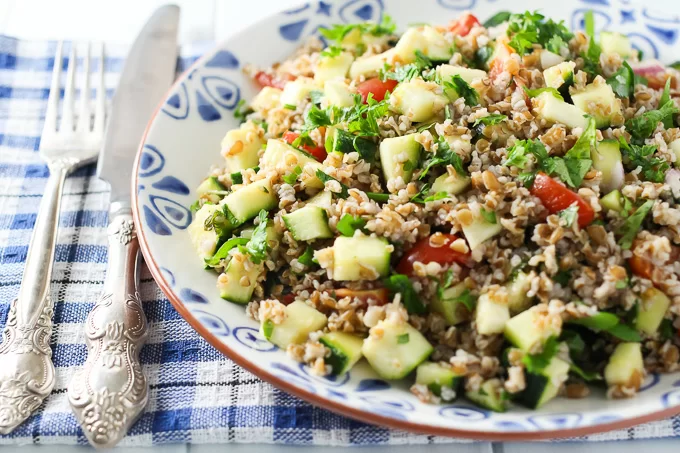 Zucchini tabbouleh salad on a plate with a fork and knife on the left side.