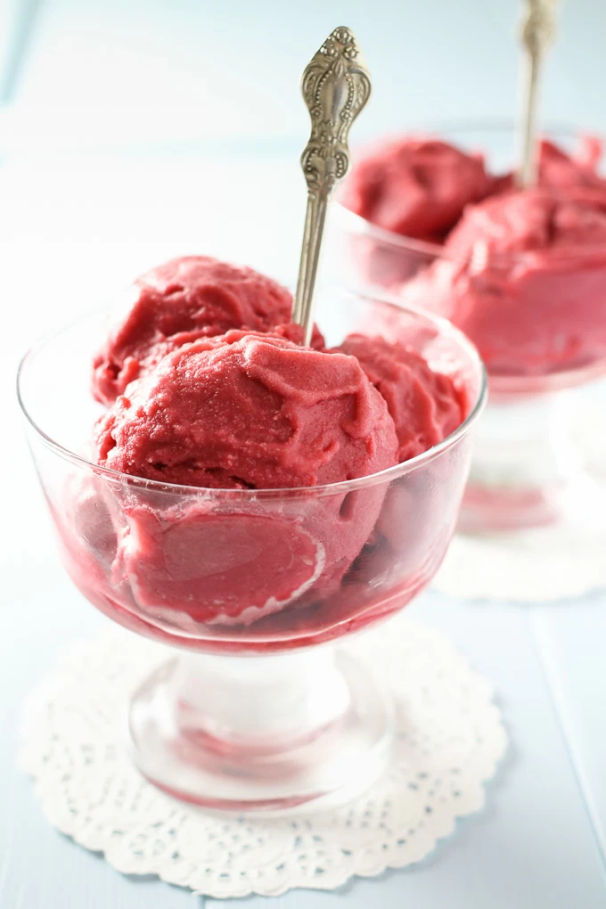 Vegan raspberry ice cream in a glass with a silver spoon in it.