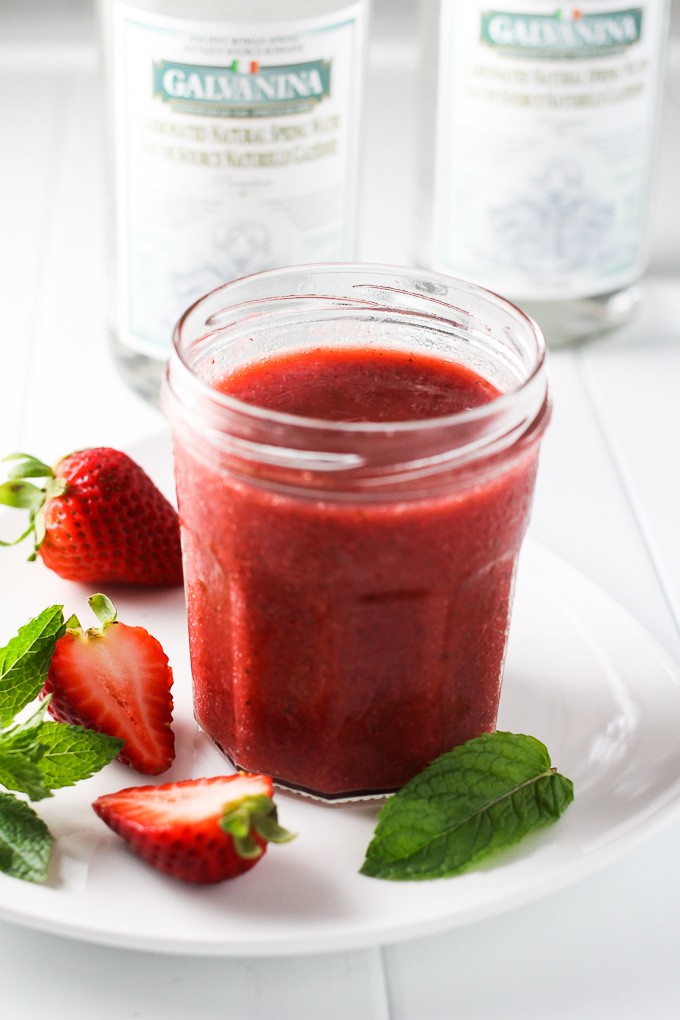 Strawberry concentrate syrup in a jar on a white plate.