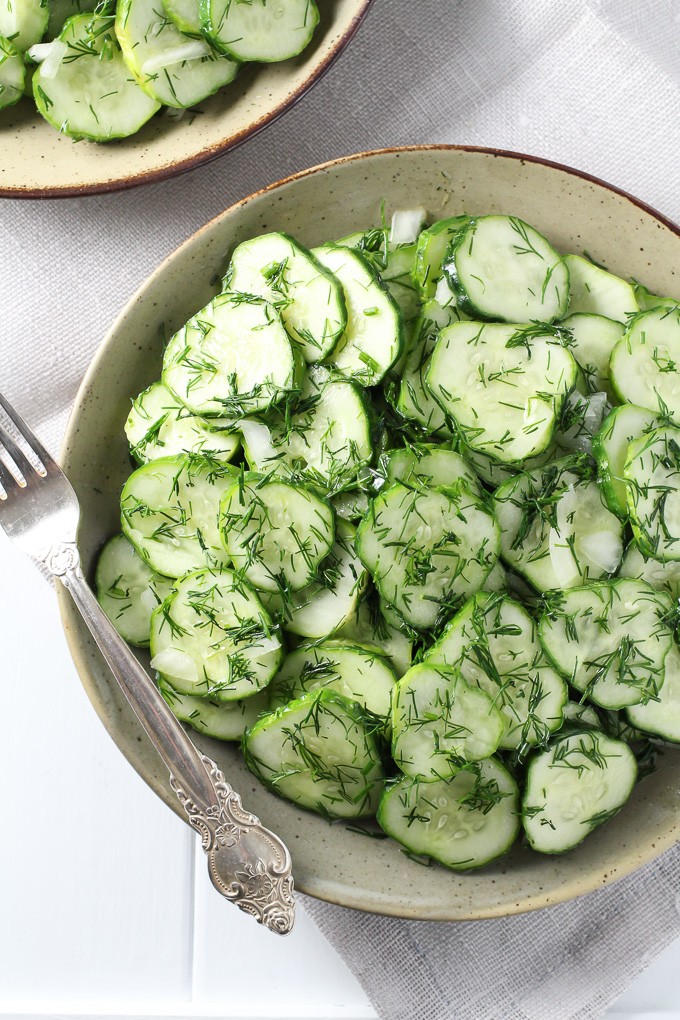 German cucumber salad on a plate with a silver fork on the left.
