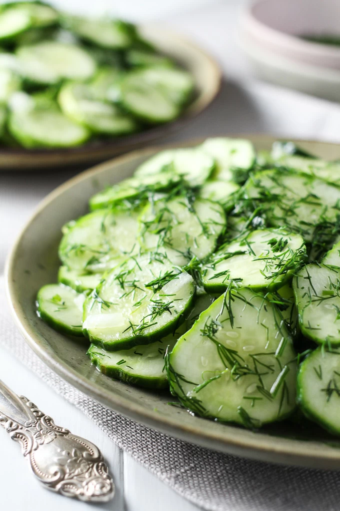 German cucumber salad on a plate garnished with chopped dill.