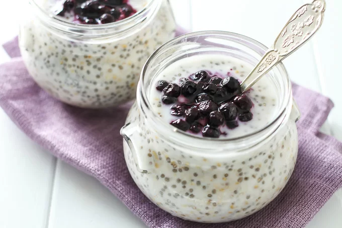Two jars with overnight steel cut oats topped with blueberries. A silver spoon is in one of the jars.