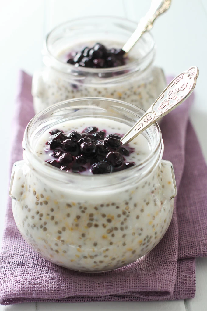 Overnight steel cut oats in two jars standing on a purple tea towel. The oats are topped with blueberries.