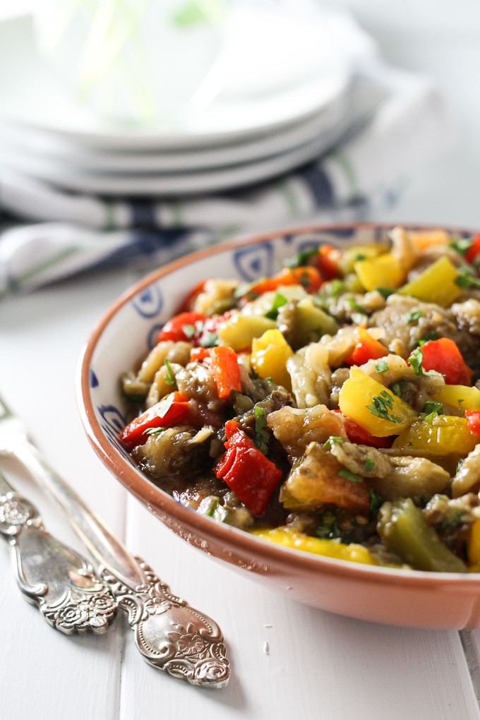 Mediterranean roasted eggplant salad in a bowl with two silver forks to the left. White plates in the background.