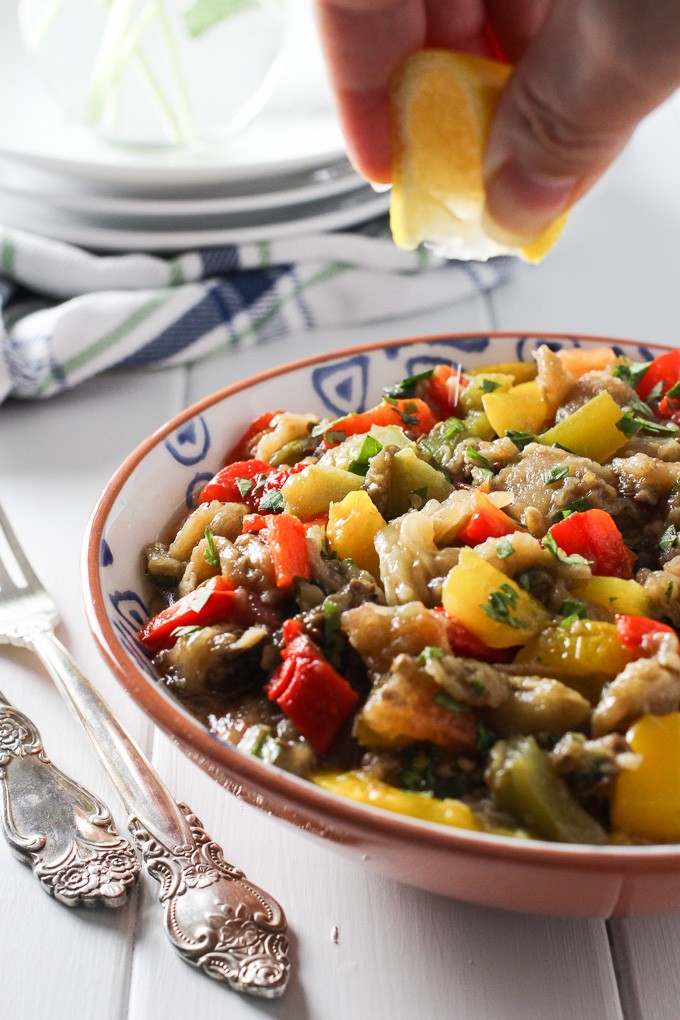 Mediterranean roasted eggplant salad in a bowl with a lemon slice being squeezed over it.