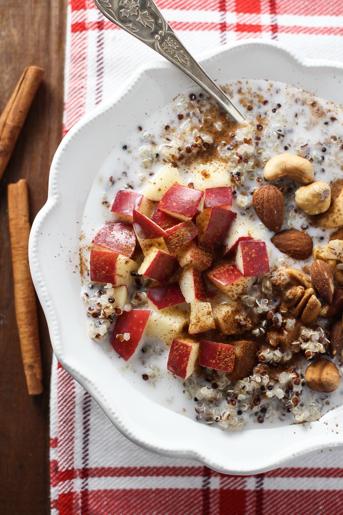 Top view of the Apple Cinnamon Quinoa Breakfast Bowl with a silver spoon in it and two cinnamon sticks on the left.