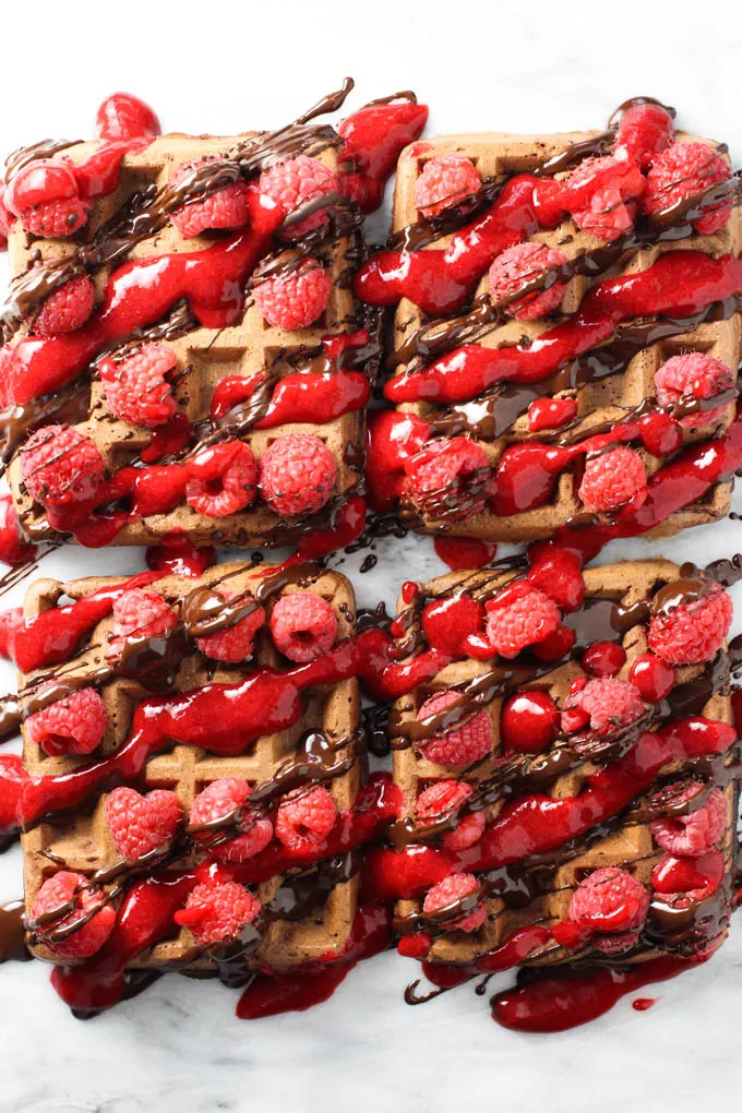 Chocolate waffles drizzled with raspberry sauce and melted chocolate and decorated with fresh raspberries.