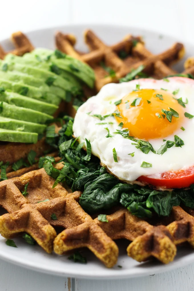 Close-up side view of a Sweet Potato Waffle topped with a fried egg, spinach and avocado.