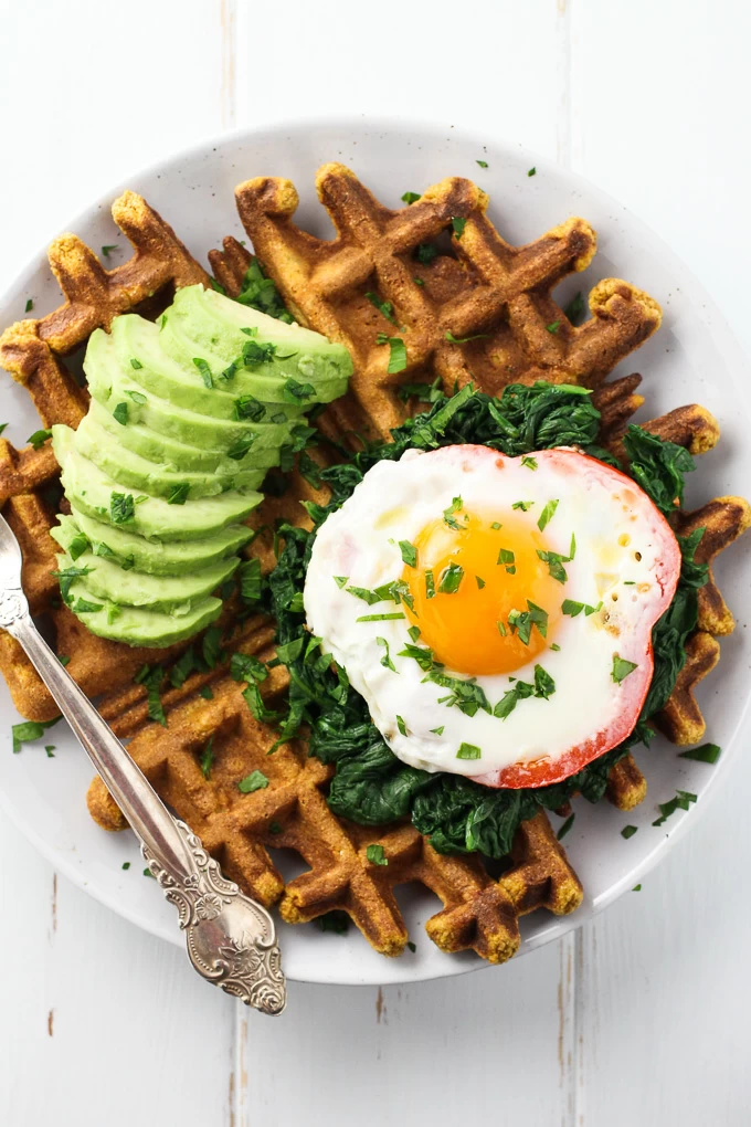 Top view of a Sweet Potato Waffle topped with a fried egg, spinach and a few avocado slices.