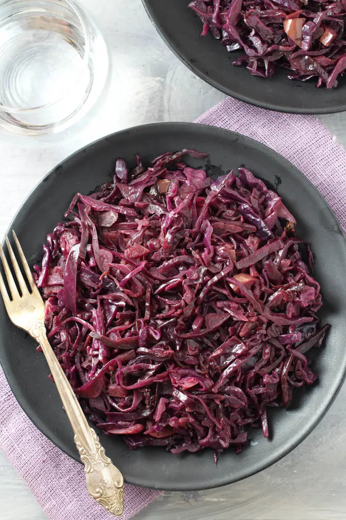 Top view of the German red cabbage on a plate standing on a purple napkin. A silver spoon on the left side.