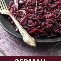 Braised red cabbage on a black plate with a silver spoon on the left side. Under the image, there is text saying German Red Cabbage with Apples.