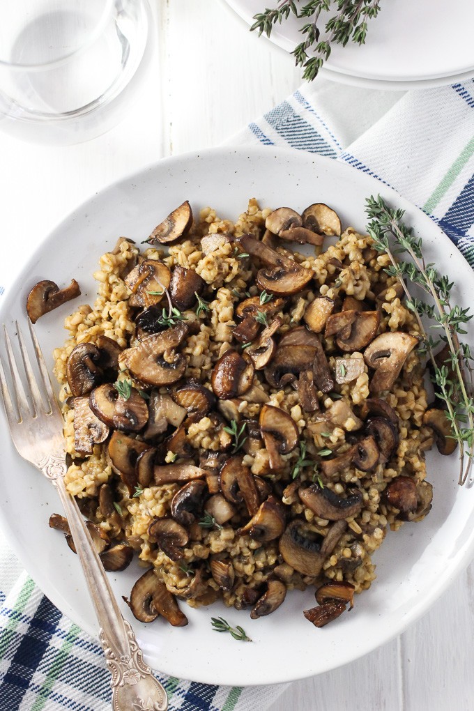 Savory Steel Cut Oats on a white plate with thyme sprig on the right and a silver fork on the left.