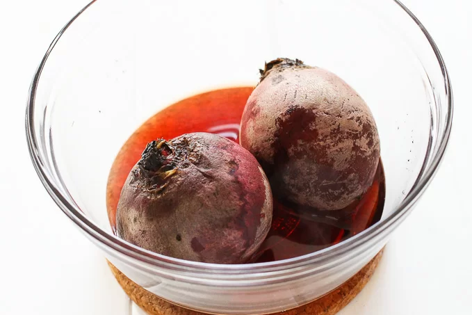 Two beets in a glass bowl with some liquid on the bottom of the bowl.