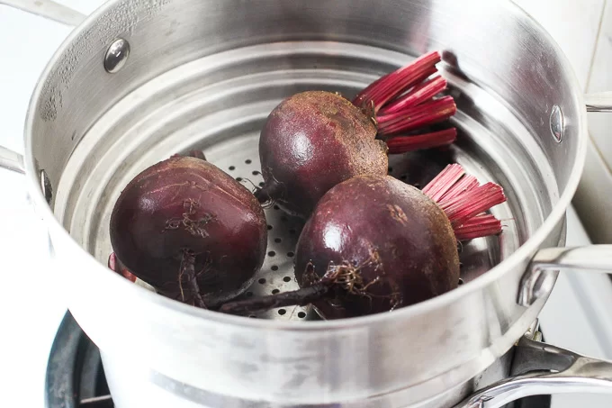 Three small beets in a steamer basket.