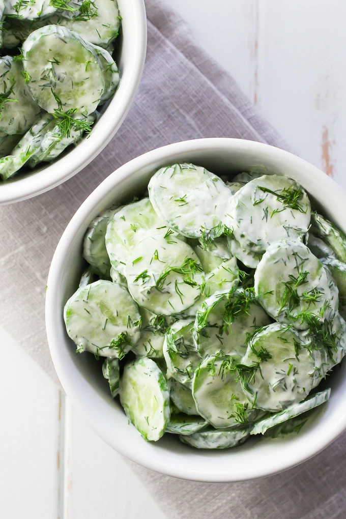 German cucumber salad with creamy dressing in a white bowl.