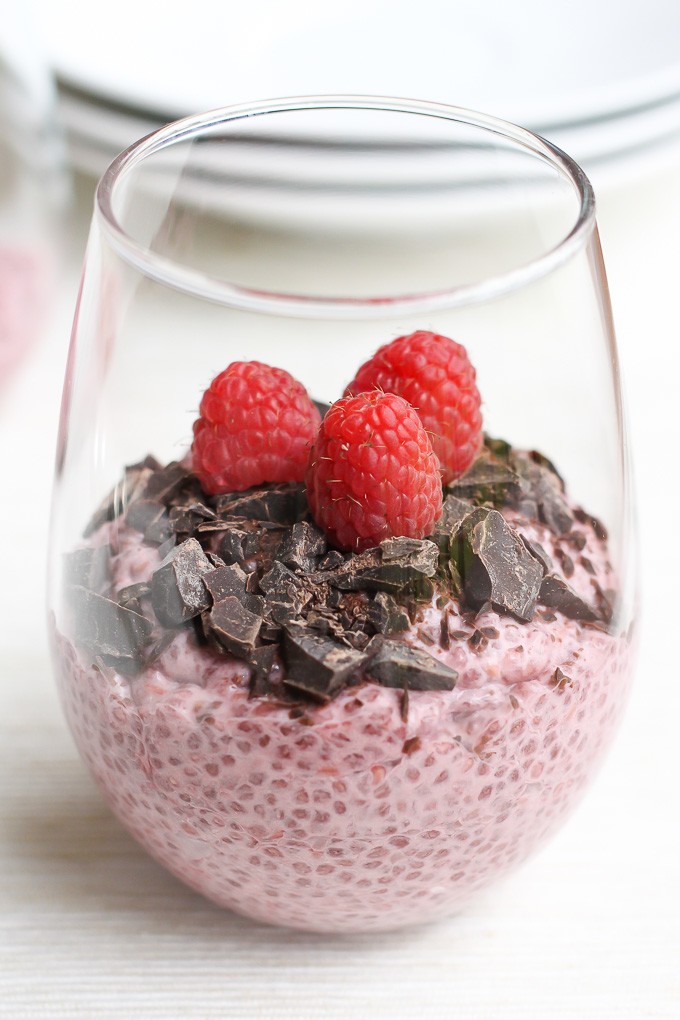 Raspberry chia pudding in a glass decorated with chocolate chunks and raspberries.