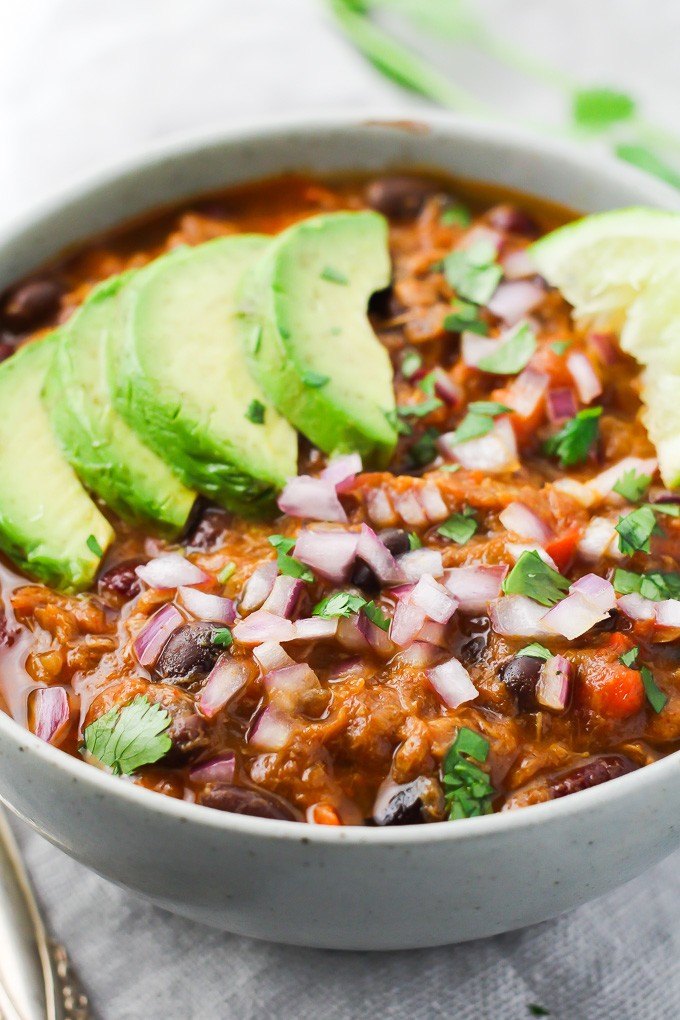 Tuna chili in a bowl garnished with avocado slices and red onion.