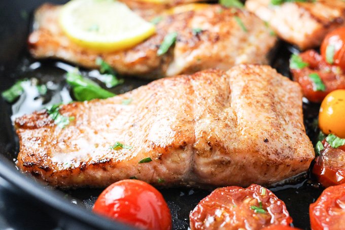 A close-up side view of a pan-fried rainbow trout slice with red cherry tomatoes.