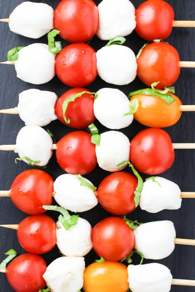 A top-view of small mozzarella cheese balls and cherry tomatoes arranged on toothpicks.
