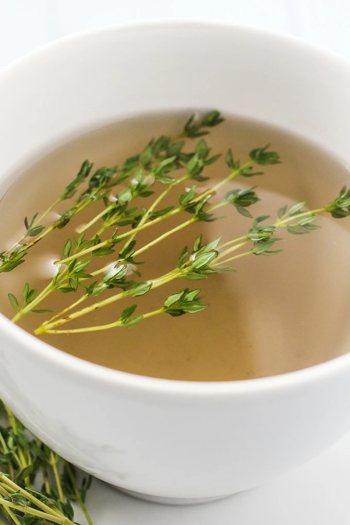 A side-view of a white teacup with the thyme tea and a few thyme sprigs in it.
