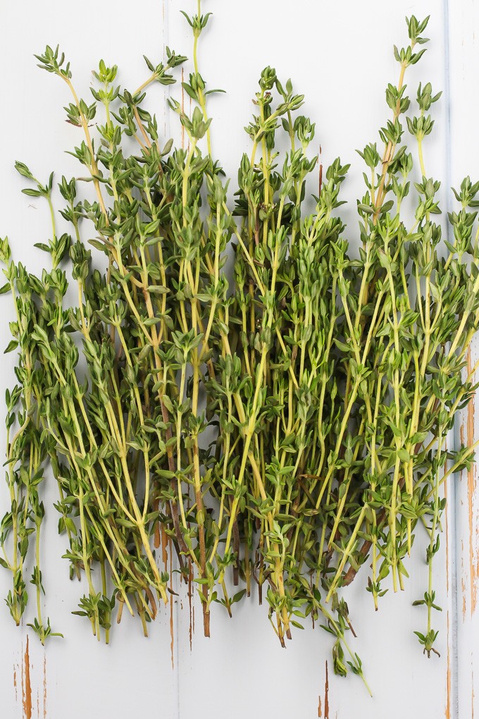 Top-view of green fresh thyme sprigs on a white wooden background.