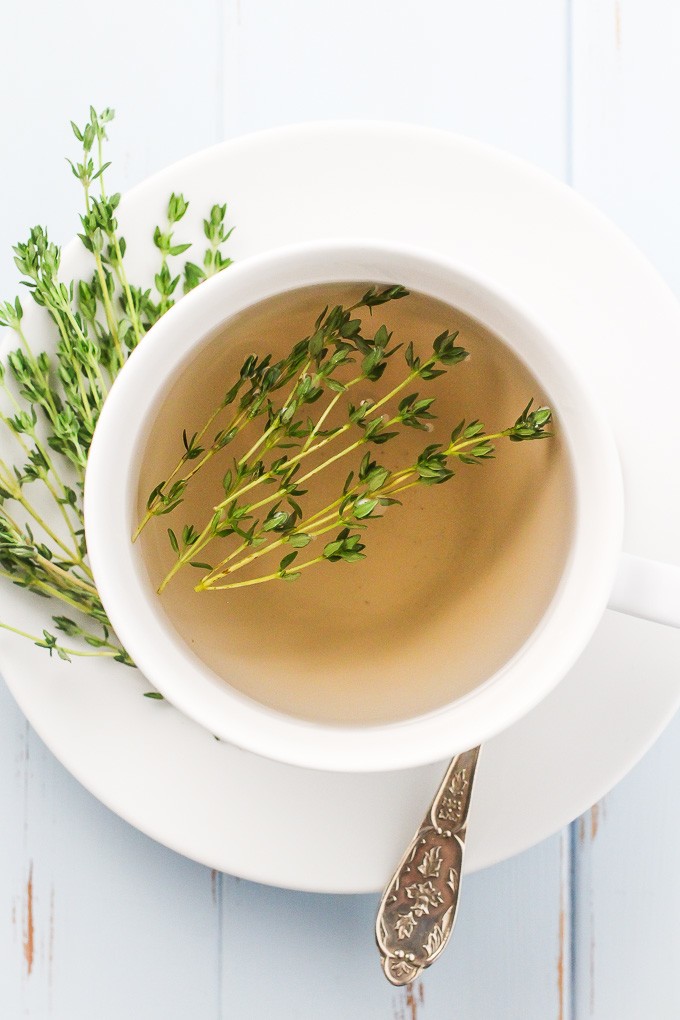 How to Make Thyme Tea: Top-view of a white teacup with a thyme tea in it standing on a white saucer.