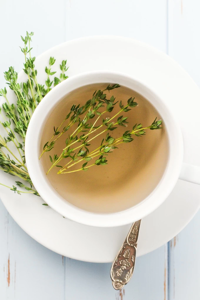 Top-view of a white teacup with a thyme tea in it standing on a white saucer.